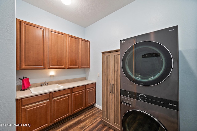 clothes washing area with sink, cabinets, dark hardwood / wood-style floors, a textured ceiling, and stacked washer / drying machine