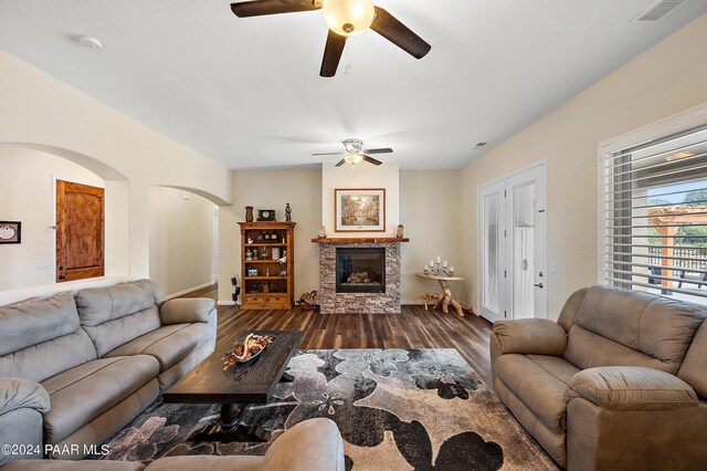 living room featuring a stone fireplace, ceiling fan, and dark wood-type flooring