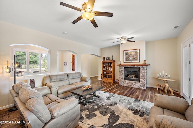 living room with dark hardwood / wood-style floors, a stone fireplace, and ceiling fan