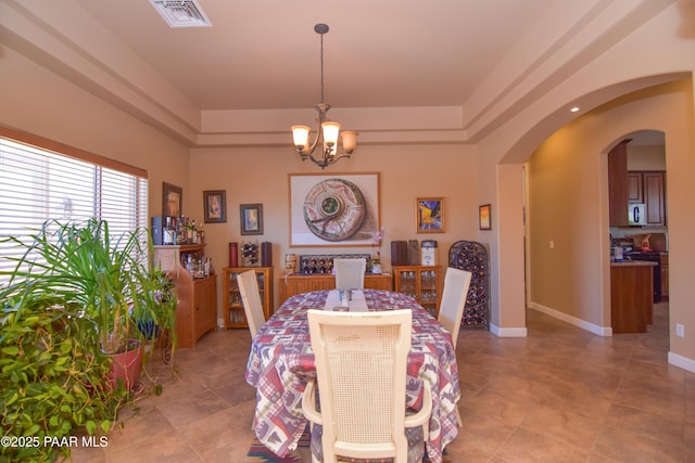 dining space featuring a chandelier, arched walkways, a tray ceiling, and light tile patterned flooring
