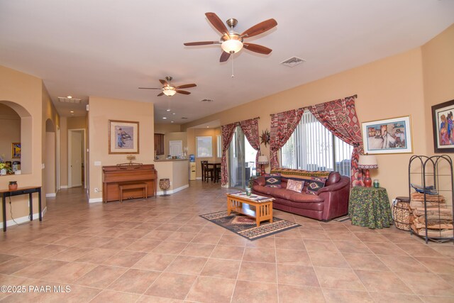 living room featuring a ceiling fan, light tile patterned flooring, arched walkways, and baseboards