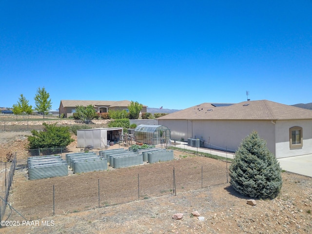 view of yard featuring a vegetable garden, a greenhouse, an outbuilding, and central AC unit