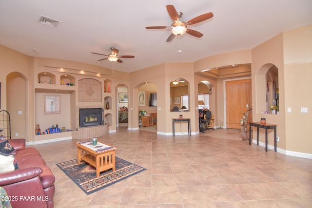living room with light tile patterned flooring, ceiling fan, arched walkways, and a fireplace