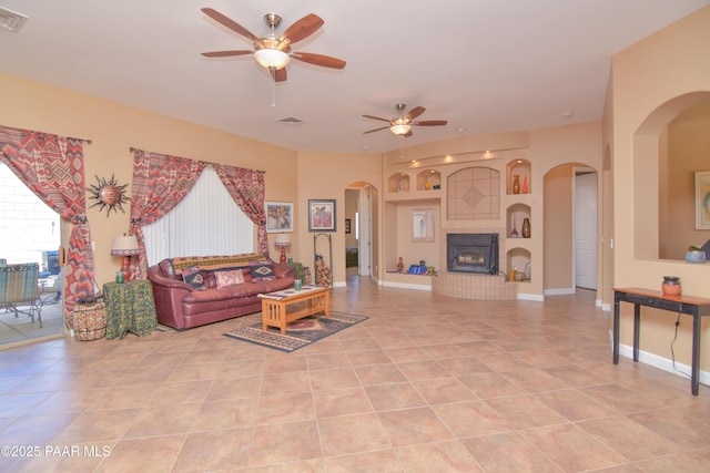 living area featuring ceiling fan, arched walkways, built in shelves, and light tile patterned flooring