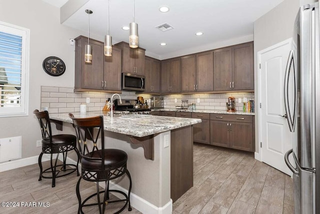 kitchen featuring kitchen peninsula, light hardwood / wood-style floors, decorative light fixtures, a breakfast bar, and appliances with stainless steel finishes