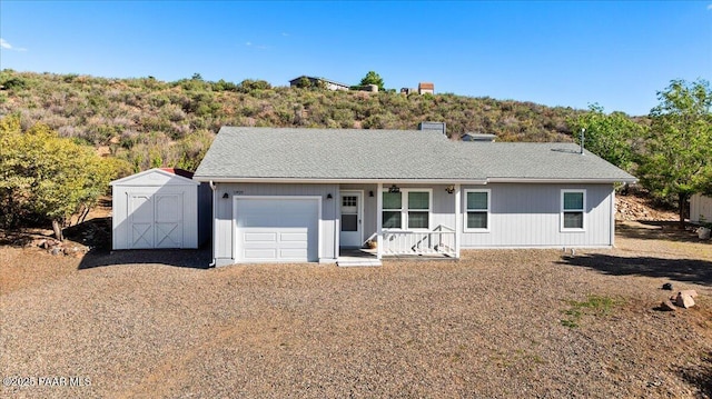 ranch-style home featuring a porch, a storage unit, an attached garage, and an outdoor structure