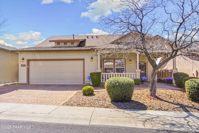 view of front of home featuring covered porch, an attached garage, decorative driveway, and roof with shingles