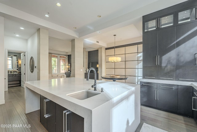 kitchen featuring a large island with sink, sink, hanging light fixtures, a notable chandelier, and a tray ceiling