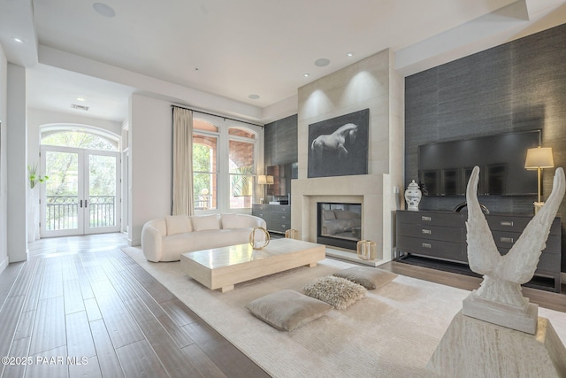 living room featuring wood-type flooring, french doors, and a large fireplace