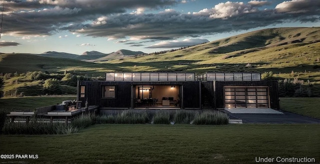 back house at dusk featuring a garage, a mountain view, and a lawn