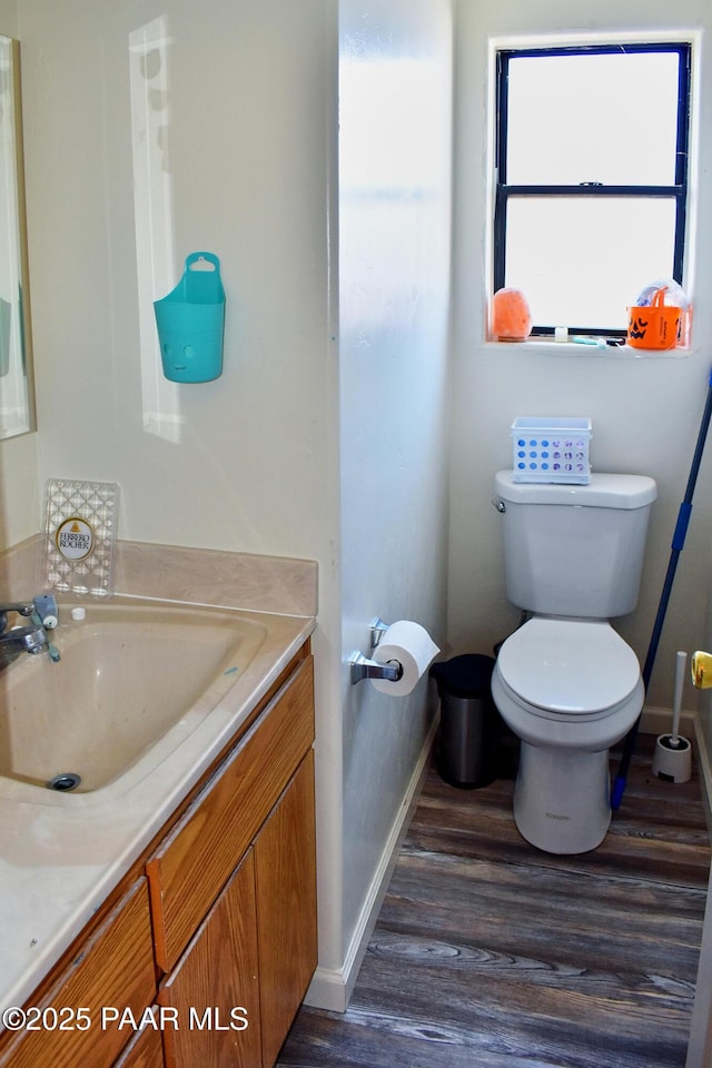 bathroom featuring baseboards, toilet, wood finished floors, and vanity