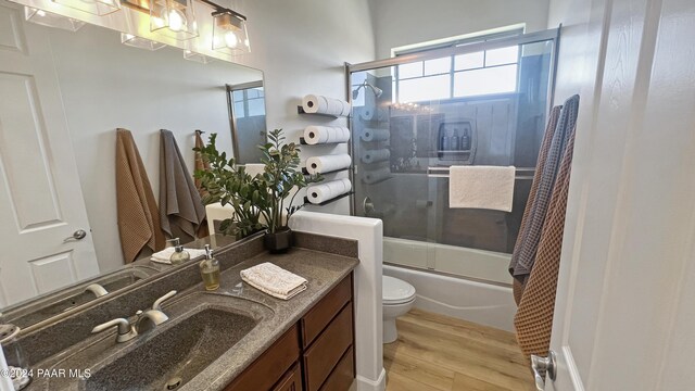 full bathroom with hardwood / wood-style floors, vanity, bath / shower combo with glass door, and toilet