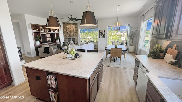 kitchen featuring a center island, hanging light fixtures, a stone fireplace, light hardwood / wood-style flooring, and ceiling fan with notable chandelier
