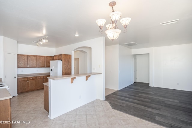 kitchen with a notable chandelier, white fridge with ice dispenser, a kitchen bar, decorative light fixtures, and kitchen peninsula