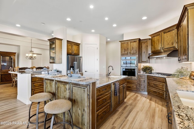 1032 Vantage Point Cir, Prescott, AZ 86301 - kitchen with appliances with stainless steel finishes, light wood-type flooring, an island with sink, a breakfast bar, and under cabinet range hood