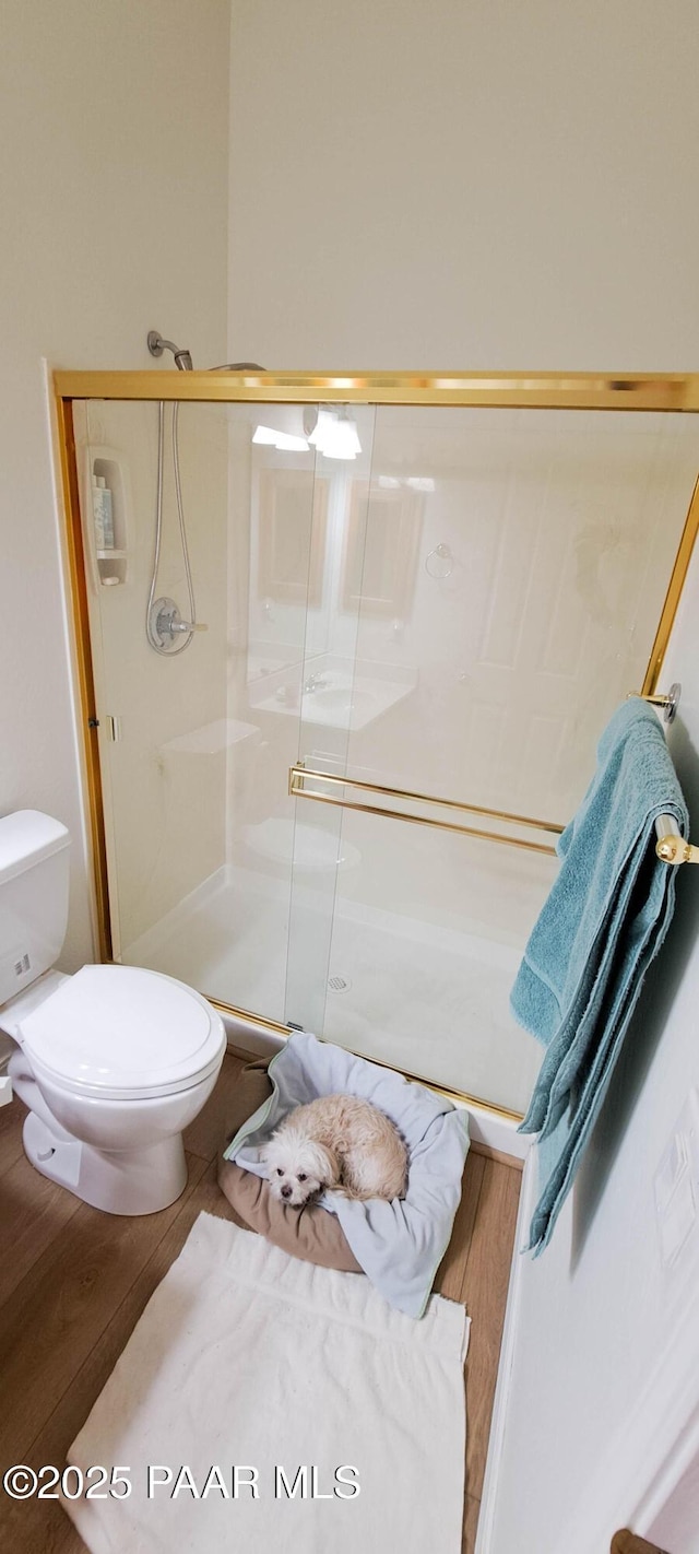 bathroom with wood-type flooring, a shower with shower door, and toilet