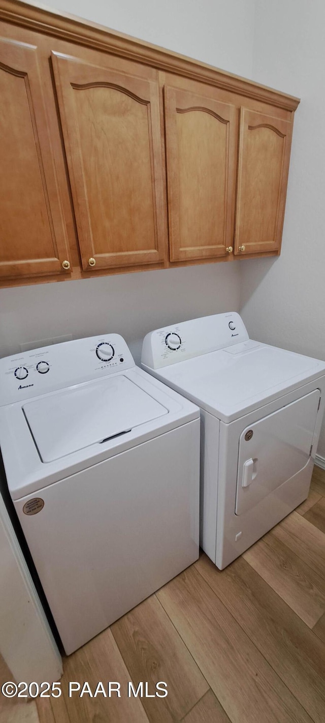 clothes washing area with washing machine and clothes dryer, cabinets, and light hardwood / wood-style floors