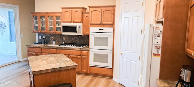 kitchen featuring decorative backsplash, a center island, white appliances, and light wood-type flooring