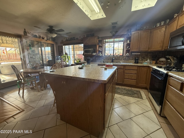 kitchen featuring ceiling fan, backsplash, a kitchen island, light tile patterned flooring, and range with gas cooktop