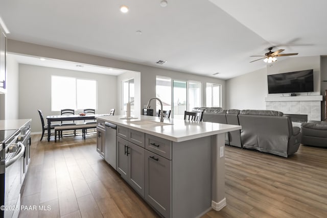 kitchen with sink, gray cabinetry, stainless steel appliances, an island with sink, and dark hardwood / wood-style flooring