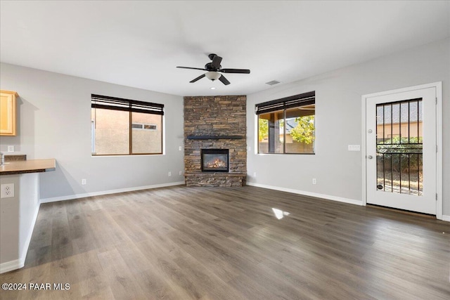 unfurnished living room with a stone fireplace, ceiling fan, and dark hardwood / wood-style floors