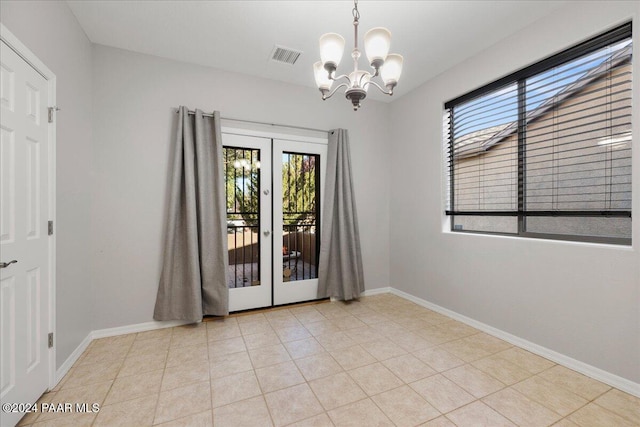 spare room featuring a notable chandelier, light tile patterned flooring, and french doors