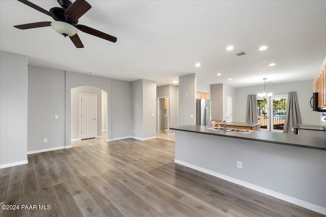 kitchen with hardwood / wood-style flooring, ceiling fan with notable chandelier, stainless steel fridge, and hanging light fixtures