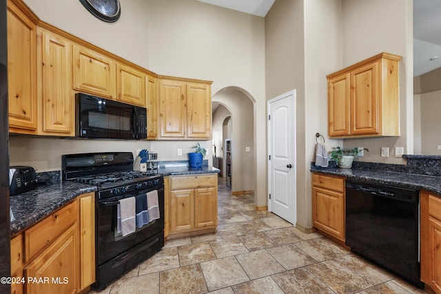 kitchen with dark stone countertops, black appliances, and a high ceiling