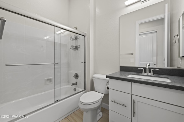 full bathroom with hardwood / wood-style flooring, vanity, toilet, and bath / shower combo with glass door