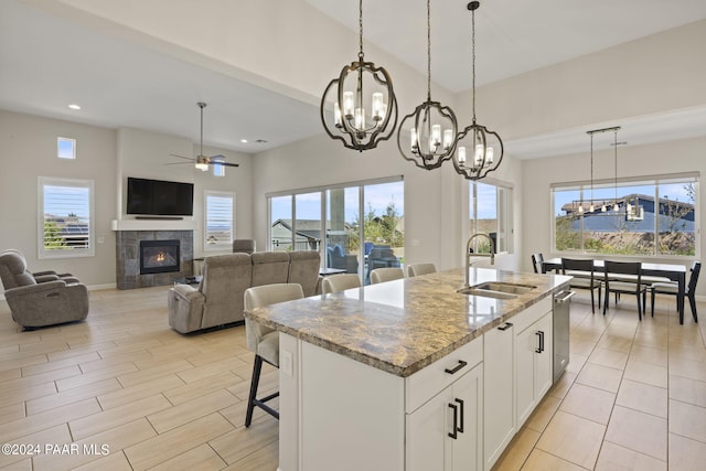 kitchen featuring light stone countertops, sink, a center island with sink, white cabinetry, and a tiled fireplace