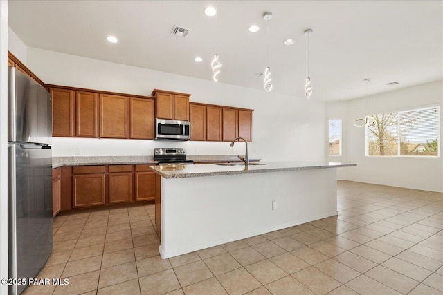 kitchen with light tile patterned floors, stainless steel appliances, a sink, pendant lighting, and brown cabinets