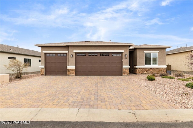 prairie-style house featuring decorative driveway, stucco siding, an attached garage, and stone siding