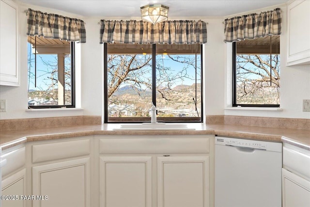 kitchen with a sink, white cabinets, white dishwasher, and light countertops