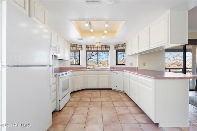 kitchen with a tray ceiling, white appliances, light tile patterned flooring, and white cabinetry