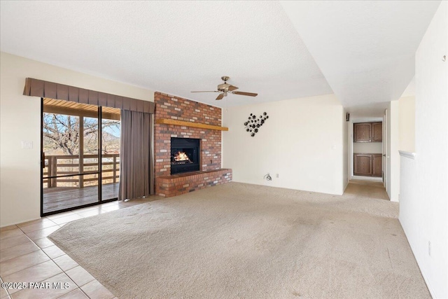 unfurnished living room with a textured ceiling, carpet, tile patterned flooring, a brick fireplace, and ceiling fan