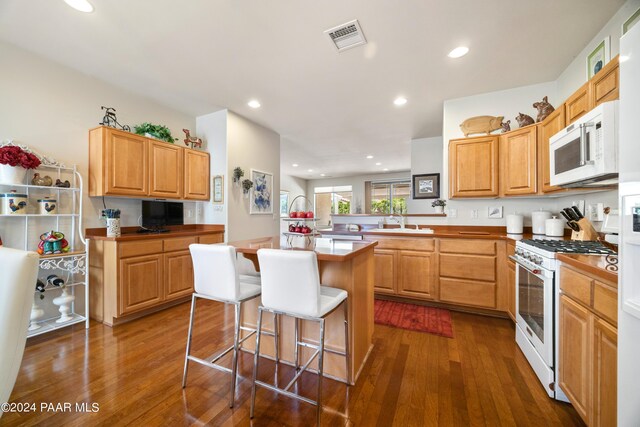 kitchen with a center island, dark hardwood / wood-style flooring, kitchen peninsula, white appliances, and a kitchen bar