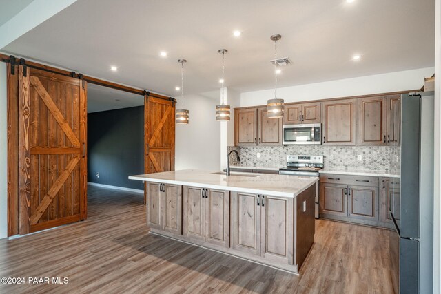 kitchen with decorative backsplash, a barn door, wood finished floors, a sink, and stainless steel appliances