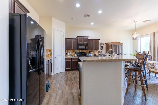 kitchen featuring light wood-style floors, light countertops, black appliances, dark brown cabinets, and visible vents