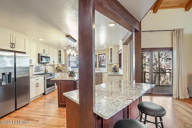 kitchen featuring a breakfast bar area, decorative light fixtures, a kitchen island, stainless steel appliances, and light stone countertops