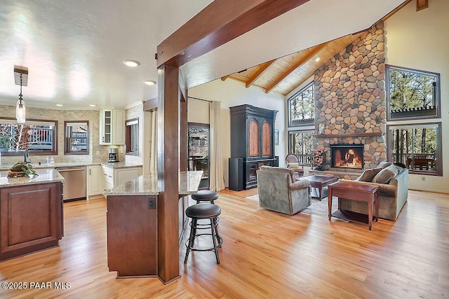 kitchen with beamed ceiling, stainless steel dishwasher, a fireplace, and light wood-type flooring