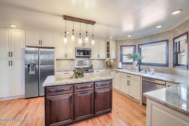 kitchen with appliances with stainless steel finishes, white cabinetry, sink, hanging light fixtures, and light hardwood / wood-style floors