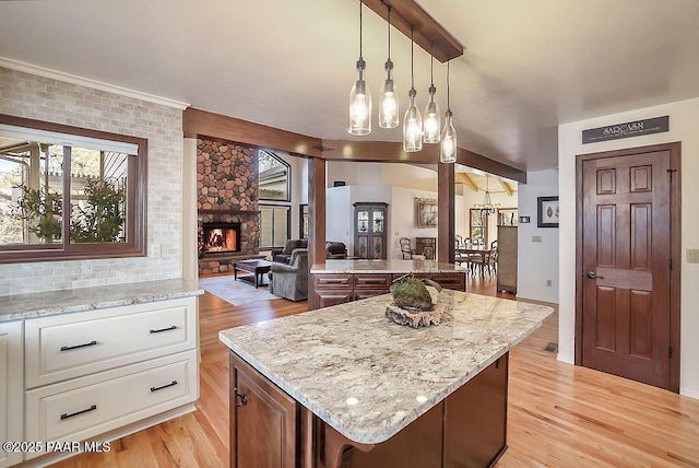 kitchen with white cabinetry, a stone fireplace, a kitchen island, and light wood-type flooring