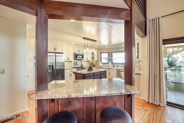 kitchen featuring backsplash, stainless steel appliances, light stone counters, a kitchen island, and decorative light fixtures