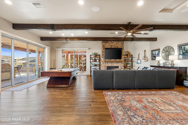 living room featuring hardwood / wood-style flooring, a stone fireplace, and beamed ceiling