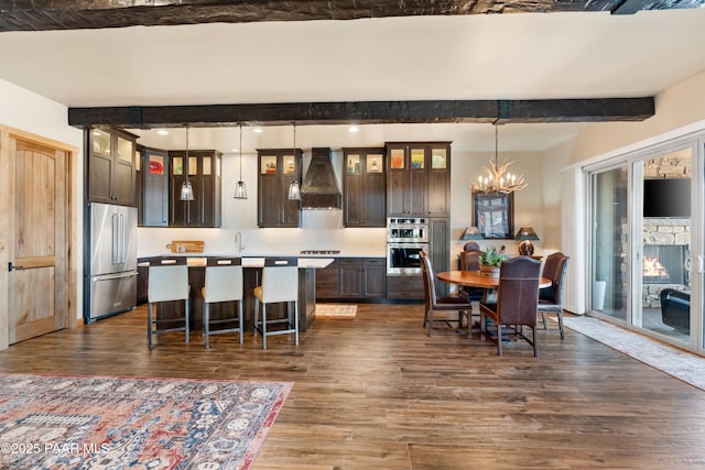 kitchen featuring dark wood-type flooring, premium range hood, hanging light fixtures, stainless steel appliances, and dark brown cabinetry