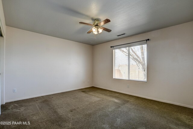 empty room featuring a ceiling fan, visible vents, dark colored carpet, and baseboards