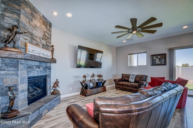 living room featuring ceiling fan, a stone fireplace, and light hardwood / wood-style flooring