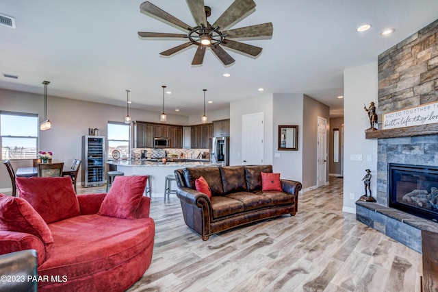 living room with a fireplace, wine cooler, light hardwood / wood-style flooring, and ceiling fan