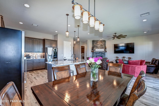 dining space with light hardwood / wood-style floors, a stone fireplace, ceiling fan, and sink