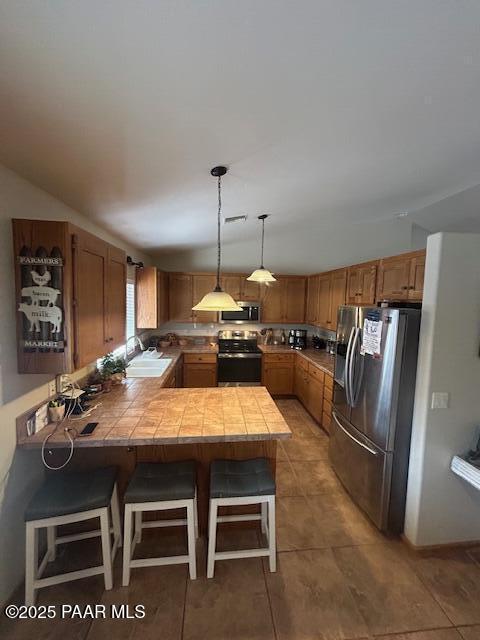 kitchen with sink, hanging light fixtures, stainless steel appliances, a kitchen breakfast bar, and kitchen peninsula